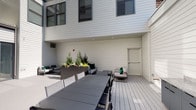 This contemporary single-floor space blends thoughtful interior design with a well-appointed outdoor area. The exterior deck, finished with grey composite decking, is enclosed by clean white lap-siding walls and features recessed overhead lighting, raised planter beds with lush greenery and seasonal blooms, and distinct zones for both dining and lounge seating — making it a versatile outdoor retreat. Large black-framed glass doors connect the interior to the deck, allowing abundant natural light to flow inward.

Inside, polished concrete floors run throughout, lending an industrial yet refined character to the space. The lobby or entry area features a bold, graphic wall mural in black, white, and green tones, paired with a wooden high-top bar table and green upholstered stools — creating a welcoming and visually dynamic first impression.

Further into the space, glass-partitioned rooms provide semi-private offices or meeting areas. These rooms are distinguished by textured accent walls, ample natural light from exterior-facing windows, and curated furnishings including ergonomic seating and statement artwork. Clean white trim and framing around the glass panels add a polished finish. Recessed ceiling lighting throughout ensures consistent illumination across all areas, contributing to a bright, professional, and creative ambiance overall.