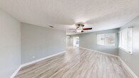 This single-floor unit offers a thoughtfully organized layout encompassing three bedrooms, three bathrooms, a living room, dining room, kitchen, hallway, laundry area, and two balconies. The open living and dining area is finished with light-toned wood-look flooring, soft sage-green walls, and a textured ceiling. A ceiling fan with a light fixture anchors the living space, while a chandelier marks the dining area. Sliding glass doors lead to one of the two balconies, allowing for natural light and outdoor access. The kitchen features a galley-style design with rich, warm wood cabinetry, granite-look countertops, stainless steel appliances, a double sink, and a recessed ceiling detail that adds dimension. The three bedrooms continue the cohesive flooring and wall palette, with the primary bedroom offering a generous footprint, natural light from windows with blinds, and a ceiling fan. Each bedroom includes access to a dedicated closet. The bathrooms carry the same warm wood vanity cabinetry and granite-look countertops seen in the kitchen, maintaining a consistent design language. Clean white trim and neutral tones throughout create a bright, cohesive, and functional living environment.
