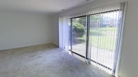 This two-floor residence offers a comfortable and functional layout designed to make the most of its natural surroundings. The main living area is finished with plush wall-to-wall carpeting that adds warmth underfoot, while clean, neutral-toned walls provide a versatile backdrop suitable for a variety of interior styles. A standout feature of the living space is the expansive sliding glass door framed by vertical blinds, which floods the room with abundant natural light and offers a direct view of the lush, green outdoor area beyond. The sliding door opens onto a patio, seamlessly connecting the interior to the exterior and creating an inviting indoor-outdoor flow. The greenery visible through the glass — including mature trees and a well-maintained lawn — enhances the sense of tranquility and connection to nature. The overall ambiance of the main level is bright, airy, and open, making it a welcoming environment for both everyday living and entertaining. Spanning two floors, the home provides ample space for a variety of living arrangements, with the upper level offering additional privacy and separation from the main living areas below.