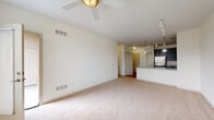 This single-floor residence offers a thoughtfully designed open-concept layout that seamlessly connects the living area to the kitchen. The spacious living room features soft neutral carpeting, a ceiling fan, and track lighting, creating a bright and airy atmosphere. Large windows in the bedroom area allow natural light to filter in, further enhancing the open feel of the space.

The kitchen is a functional highlight, equipped with stainless steel appliances including a gas range, built-in microwave, and refrigerator. Rich dark cabinetry contrasts elegantly with granite-style countertops, and a peninsula with pendant lighting provides both additional workspace and a casual dining option. Hardwood-style flooring runs throughout the kitchen, adding warmth and easy maintenance.

The residence includes two bathrooms. The full bathroom features a tiled tub-shower combination with chrome fixtures and tile flooring, while the second bathroom offers a dark-cabineted vanity with a white countertop, a large mirror, and tile flooring. The bedrooms are generously sized, finished with plush carpeting and clean white walls, offering a calm and comfortable retreat. Overall, the space presents a clean, neutral palette throughout, making it highly versatile and move-in ready.