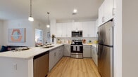 Located at 820 Clawson Place in Fort Mill, South Carolina, this single-floor residence offers a thoughtfully designed layout with contemporary finishes and functional living spaces throughout. The kitchen is a standout feature, showcasing a U-shaped configuration with two-tone cabinetry — white upper cabinets paired with grey lower cabinets — complemented by white quartz countertops, a subway tile backsplash, and a full suite of stainless steel appliances including a refrigerator, range, microwave, and dishwasher. Light wood-style flooring extends through the kitchen and into the open living area, which is filled with natural light from large windows dressed with sheer curtains and blinds. The living room offers a comfortable, open feel with a ceiling fan and direct access to additional natural light. The bedrooms feature plush carpeting, generous windows, and ceiling fans, creating restful retreats. The primary bedroom is complemented by a well-proportioned en-suite bathroom featuring light wood flooring, a sliding glass shower enclosure, and direct access to a spacious walk-in closet with built-in wire shelving. Additional bedrooms are served by their own closet space. Throughout the residence, a neutral color palette and clean architectural lines contribute to a cohesive, modern aesthetic.