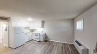 This single-floor unit offers a straightforward, functional layout designed for comfortable everyday living. The open-concept living and kitchen area is unified by durable wood-look laminate flooring in a neutral grey-brown tone, creating a cohesive and easy-to-maintain interior throughout.

The kitchen is efficiently arranged in an L-shaped configuration and includes white cabinetry with ample upper and lower storage, light granite-style countertops, a double stainless steel sink, a white electric coil range, and a full-size white refrigerator. Under-cabinet lighting provides added visibility for meal preparation.

The living area is bright and open, featuring two windows fitted with blinds that allow natural light to filter in, along with a wall-mounted PTAC heating and cooling unit for year-round climate control. A white entry door with a sidelight panel provides direct access to the unit.

The bedroom is a quiet, well-proportioned room with wood-look flooring and a window offering natural light. Neutral wall tones throughout the unit contribute to a calm, clean aesthetic.

The bathroom is equipped with a full-size soaking tub and shower combo featuring a white surround and chrome fixtures, maintaining the unit's clean and functional character. Overall, the space presents a neat, move-in-ready environment with a practical and cohesive design.