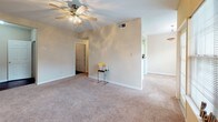 This single-floor residence offers a practical and comfortable layout spread across multiple rooms. The living area features neutral-toned walls, plush wall-to-wall carpeting, and a ceiling fan with integrated lighting, creating a bright and airy atmosphere. Natural light filters in through windows fitted with blinds, offering views of surrounding greenery. The space flows openly toward the kitchen via a pass-through opening.

The galley-style kitchen is well-equipped with black appliances, including a refrigerator, range, and over-the-range microwave. White cabinetry lines both sides of the kitchen, providing ample storage, while durable wood-look flooring runs the length of the space. A breakfast bar counter connects the kitchen to the adjacent living area, adding functionality.

The bedrooms continue the warm, neutral aesthetic with soft carpeting, ceiling fans, and windows that bring in natural light. Each room offers a comfortable footprint suitable for standard furnishings. The bathroom includes a tub and shower combination, a vanity with light countertops, white cabinetry, dark wood-look flooring, and a large mirror above the sink. The overall ambiance of the unit is clean, functional, and move-in ready.