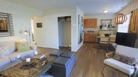 This single-floor residence offers a thoughtfully designed layout that blends comfort and functionality. The open-concept living area serves as the heart of the home, featuring rich hardwood-style flooring that flows seamlessly throughout the space, creating a warm and cohesive aesthetic.

The living room is generously sized, providing ample room for seating arrangements and everyday living. A standout feature is the large built-in closet with double doors, offering substantial storage space that keeps the living area organized and clutter-free. A partial wall divider elegantly separates the living space from the rest of the unit while maintaining an open, airy feel.

Adjacent to the living area, the kitchen is equipped with warm honey-toned wood cabinetry that provides plentiful storage. The space accommodates a dining area, making it ideal for casual meals and entertaining. The kitchen's layout is practical and efficient, with counter space suited for everyday meal preparation.

Natural light filters through the space, contributing to a bright and welcoming ambiance. The neutral wall tones complement the flooring and cabinetry, creating a versatile backdrop that suits a variety of interior styles. Overall, this residence delivers a functional, comfortable living environment with practical storage solutions and a cohesive design throughout.