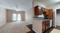 This single-floor, one-bedroom, one-bathroom unit offers a practical and comfortable layout designed for efficient everyday living. The living area is generously sized, featuring soft wall-to-wall carpeting, crown molding, and a ceiling fan overhead. French doors flood the space with natural light and provide direct access to an outdoor area, creating a bright and airy atmosphere.

The kitchen is designed in a galley style, offering rich warm-toned wood cabinetry, dark granite-style countertops, and dark hardwood flooring. A peninsula counter opens toward the living area, making it ideal for casual dining or entertaining. Black appliances, including a full-size refrigerator, complement the cabinetry and add a cohesive, modern touch.

The entryway transitions smoothly between the hardwood flooring of the kitchen and the carpeted living and bedroom areas. The bedroom is a comfortable, well-proportioned room with plush carpeting, a ceiling fan, and a window that allows in natural light.

The bathroom is finished with dark hardwood-style flooring and features warm wood vanity cabinetry, a single-sink countertop, and a full tub-shower combination. Crown molding and neutral warm-beige tones carry throughout the unit, contributing to a cohesive and inviting overall aesthetic.