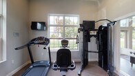 Located at 941 Taylor Station Rd in Gahanna, Ohio, this single-floor property offers a practical and well-appointed layout designed to accommodate both everyday living and active lifestyles. The standout feature of this space is a dedicated fitness room, thoughtfully equipped with a full complement of exercise machines including a treadmill, stationary bike, and a multi-function cable weight training system. A large, grid-paned window fills the room with natural light and provides pleasant views of the surrounding greenery, creating an inviting environment for workouts. A wall-mounted television adds a convenient entertainment option during exercise sessions. The neutral-toned walls and carpeted flooring contribute to a clean, functional aesthetic throughout the fitness area. Additional rooms in the property, while dimly lit in available imagery, feature windowed walls with horizontal blinds, suggesting consistent natural light access throughout the space. The overall layout reflects a straightforward, single-level design that prioritizes usability and comfort. Situated in the Gahanna community of central Ohio, this property combines suburban surroundings with purposeful interior features suited for an active and comfortable daily routine.