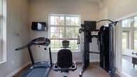 Located at 941 Taylor Station Rd in Gahanna, Ohio, this single-floor property offers a practical and well-appointed layout designed to accommodate both everyday living and active lifestyles. The standout feature of this space is a dedicated fitness room, thoughtfully equipped with a full complement of exercise machines including a treadmill, stationary bike, and a multi-function cable weight training system. A large, grid-paned window fills the room with natural light and provides pleasant views of the surrounding greenery, creating an inviting environment for workouts. A wall-mounted television adds a convenient entertainment option during exercise sessions. The neutral-toned walls and carpeted flooring contribute to a clean, functional aesthetic throughout the fitness area. Additional rooms in the property, while dimly lit in available imagery, feature windowed walls with horizontal blinds, suggesting consistent natural light access throughout the space. The overall layout reflects a straightforward, single-level design that prioritizes usability and comfort. Situated in the Gahanna community of central Ohio, this property combines suburban surroundings with purposeful interior features suited for an active and comfortable daily routine.