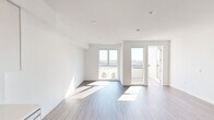 This contemporary single-floor residence showcases a clean, modern design throughout. The open-concept layout connects the living area to the kitchen, creating a cohesive and functional space. Wood-look plank flooring runs continuously throughout, complementing the crisp white walls and adding warmth to the overall aesthetic.

The kitchen is well-appointed with stainless steel appliances, including a refrigerator, electric range, and over-the-range microwave. Two-toned cabinetry pairs white upper cabinets with light wood lower cabinets, accented by white quartz countertops and a subtle vertical tile backsplash. A stainless steel sink completes the space.

The living area is generously proportioned and bathed in natural light from large floor-to-ceiling windows, which frame elevated views of the surrounding cityscape and palm trees. A private balcony is accessible directly from the living space, extending the indoor-outdoor connection.

The bedroom offers ample space with a large window providing additional city views and a well-organized reach-in closet with built-in shelving and hanging rods. A second closet is also present near the entry.

The bathroom features a soaking tub with a shower, finished with light gray large-format tile surround and brushed nickel fixtures, maintaining the unit's consistent modern palette.