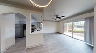 This contemporary apartment showcases an open concept design, seamlessly blending living and dining areas. The space is characterized by light wood-style flooring throughout, creating a warm and cohesive aesthetic. Multiple ceiling fans with integrated lighting fixtures ensure comfort and illumination. The kitchen boasts white cabinetry, stainless steel appliances, and a striking herringbone tile backsplash. Large windows and sliding glass doors flood the space with natural light, while a circular LED ceiling fixture adds a modern touch. The bathroom features a sleek vanity and a tiled shower with a curved curtain rod. The overall design emphasizes brightness, spaciousness, and functional elegance.