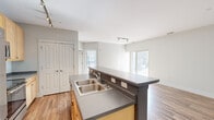 Located at 144 N Jefferson St in the heart of downtown Milwaukee, WI, this one-bedroom, one-bathroom unit offers a well-designed open-concept layout with consistent hardwood-style flooring throughout. The combined kitchen and living area forms the central hub of the space, bathed in natural light from large sliding glass doors that open to an outdoor view. Track lighting accents the living area, adding a modern touch to the neutral gray walls and clean white trim.

The kitchen is equipped with stainless steel appliances, including a refrigerator, electric range, and microwave, all complemented by light wood cabinetry and gray laminate countertops. A spacious island with a double stainless steel sink provides additional prep space and casual seating potential. A set of double doors offers convenient pantry or storage access directly off the kitchen.

The bedroom is a generously sized, sun-filled room with multiple windows fitted with horizontal blinds, offering both privacy and natural light. It connects seamlessly to a large walk-in closet outfitted with wire shelving and hanging rods for ample storage. The bathroom features a full tub-shower combo with white tile surround and brushed nickel fixtures, maintaining the unit's clean, contemporary aesthetic throughout.
