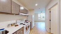 Located at 2133 North Argyle Street in Portland, Oregon, this efficiently designed studio unit offers a practical and well-organized single-floor layout. The combined kitchen and living area makes smart use of the available space, with the kitchen positioned along one wall and the open living area extending toward a large window that fills the room with natural light and offers views of the surrounding neighborhood. The kitchen is fully equipped with white appliances, including an electric range with overhead ventilation, a full-size refrigerator, and a dishwasher. Rich, dark-toned cabinetry provides ample storage above and below the clean white countertops. Light wood-look flooring runs throughout the entire unit, lending warmth and visual continuity from the kitchen through the living area. A ceiling fan with integrated lighting serves the living space, contributing to both comfort and ambiance. The bathroom features a full tub-shower combination with clean white surroundings, wood-look flooring consistent with the rest of the unit, and a vanity with matching cabinetry. Recessed lighting and a neutral color palette throughout keep the space feeling bright, clean, and open. A dedicated entryway with a closet provides additional storage and a clear transition into the living area.