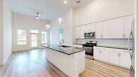 This well-designed single-story home offers two bedrooms and two bathrooms across a thoughtfully laid-out floor plan. The open-concept living and kitchen area immediately impresses with soaring ceilings, a ceiling fan, and abundant natural light streaming through large front-facing windows and a glass door. Light wood-tone flooring runs seamlessly throughout, enhancing the bright, airy ambiance.

The kitchen is a standout feature, anchored by a large center island with a dark granite countertop and undermount sink, complemented by sleek globe pendant lighting. White shaker cabinetry lines the walls, paired with a classic subway tile backsplash and a full suite of stainless steel appliances, including a gas range, built-in microwave, and refrigerator.

The primary bedroom is generously proportioned with high ceilings and direct access to a walk-in closet outfitted with wrap-around shelving and hanging rods. The en-suite primary bathroom is elegantly appointed with a dark granite vanity, large-format white tile flooring, and a glass-enclosed shower and soaking tub surrounded by marble-style tile. The second bedroom is equally bright, featuring tall ceilings and a well-sized window. Both bedrooms benefit from dedicated closet space. The second bathroom mirrors the refined finishes of the primary, with a glass-enclosed marble-tile shower and a dark granite vanity.