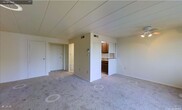 Located at 51 Grafton Avenue in Dayton, Ohio, this single-floor residence offers a straightforward and functional layout designed for comfortable everyday living. The main living area is finished with wall-to-wall carpeting in a neutral tone, creating a warm and cohesive atmosphere throughout. Light-colored walls and a paneled ceiling contribute to a clean, understated aesthetic that keeps the space feeling open and airy.

A defining feature of the layout is the partial dividing wall that separates the living area from the kitchen, incorporating a pass-through counter that maintains a sense of openness while providing a clear distinction between the two spaces. The kitchen is equipped with dark wood cabinetry and a countertop sink, offering practical storage and workspace. Louvered cabinet doors add a classic touch to the kitchen's design. Overhead HVAC vents are present throughout, ensuring climate control across the unit.

A hallway accessible from the main living area leads to additional rooms, with a visible entry door providing straightforward access. The overall layout is efficient and well-organized, making good use of the available footprint. The neutral color palette and consistent finishes throughout lend the space a cohesive, move-in-ready character suitable for a variety of living arrangements.