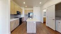 Located at 2002 S Highway 89 in Logan, Utah, this contemporary single-floor unit offers a well-designed, open-concept layout with modern finishes throughout. The kitchen serves as a central highlight, featuring a large island with a white quartz countertop and undermount sink, light wood-tone cabinetry, gray subway tile backsplash, and black appliances including a refrigerator, range, and over-the-range microwave. The kitchen flows seamlessly into the living area, which is accented by a bold teal-gray feature wall, rich wood-look vinyl plank flooring, and a ceiling fan. A sliding glass door fills the living space with natural light and provides access to a private balcony with exterior views. The unit includes a dedicated in-unit laundry area with a full-size washer and dryer. The bathroom is cleanly finished with a tub-shower combination, white tile surround, wood-tone vanity with white countertop, and a framed mirror. Recessed lighting throughout the unit ensures consistent, modern illumination. The overall design balances contemporary aesthetics with functional living, making it a practical and stylish space in the Logan, UT area.