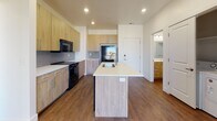 Located at 2002 S Highway 89 in Logan, Utah, this contemporary single-floor unit offers a well-designed, open-concept layout with modern finishes throughout. The kitchen serves as a central highlight, featuring a large island with a white quartz countertop and undermount sink, light wood-tone cabinetry, gray subway tile backsplash, and black appliances including a refrigerator, range, and over-the-range microwave. The kitchen flows seamlessly into the living area, which is accented by a bold teal-gray feature wall, rich wood-look vinyl plank flooring, and a ceiling fan. A sliding glass door fills the living space with natural light and provides access to a private balcony with exterior views. The unit includes a dedicated in-unit laundry area with a full-size washer and dryer. The bathroom is cleanly finished with a tub-shower combination, white tile surround, wood-tone vanity with white countertop, and a framed mirror. Recessed lighting throughout the unit ensures consistent, modern illumination. The overall design balances contemporary aesthetics with functional living, making it a practical and stylish space in the Logan, UT area.