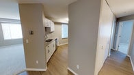 This single-floor residence offers a clean, modern aesthetic with a thoughtful layout designed for comfortable everyday living. The kitchen is a standout feature, showcasing crisp white cabinetry that extends to the upper walls, providing ample storage and a bright, airy feel. Light-toned countertops complement the cabinetry, while a classic white tile backsplash adds a subtle decorative touch. The kitchen is equipped with a stainless steel sink and dishwasher, offering both style and functionality. A window with slatted blinds allows natural light to filter into the kitchen, creating a warm and inviting atmosphere. Warm hardwood-style flooring flows seamlessly throughout the space, tying each area together with a cohesive and contemporary look. Neutral gray walls provide a versatile backdrop that complements a variety of furnishing styles. The open transitional hallway connects the kitchen to the rest of the residence, enhancing the sense of flow and openness. White baseboards and trim add a polished finishing touch throughout. Overall, the space presents a well-maintained, move-in-ready environment with a fresh, modern character.