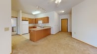 Located at 2707 Park Place Ln in Janesville, Wisconsin, this single-floor unit offers a thoughtfully designed, open layout that maximizes both functionality and comfort. The kitchen is a standout feature, equipped with warm honey-toned cabinetry, light countertops, a gas range, built-in microwave, refrigerator, and a peninsula that provides additional prep space and casual seating. Track lighting and a ceiling fan with integrated light fixture illuminate the combined kitchen and living area, which transitions seamlessly from tile flooring to plush neutral carpeting. The living area is generously sized and benefits from natural light streaming through French doors that open to an outdoor patio, offering views of the surrounding exterior. The bedrooms are carpeted and bright, each featuring windows with blinds that allow for natural light and privacy. One bedroom includes a dedicated closet, while another offers direct access to a hallway with additional storage. The bathroom is finished with large-format tile flooring, a dual-sink vanity with dark countertops and wood cabinetry, a well-lit mirror, and a shower/tub combination. Throughout the unit, warm wood-toned trim and doors provide a cohesive, classic aesthetic.
