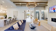 Located at 16045 East Easter Circle in Aurora, Colorado, this thoughtfully designed single-floor community space offers a sophisticated blend of modern aesthetics and functional areas. The main lounge draws immediate attention with its exposed wood beam ceiling details, light hardwood flooring, and a striking double-ring gold chandelier that serves as a bold focal point. Comfortable seating arrangements, including a deep navy sectional sofa and accent chairs, create an inviting atmosphere bathed in natural light streaming through large glass entry doors.

The kitchen and bar area is equally impressive, showcasing a bold teal herringbone tile backsplash that contrasts beautifully against crisp white cabinetry and a long quartz-topped island with bar seating. Globe pendant lighting adds a stylish finishing touch overhead.

Adjacent to the kitchen, a casual dining lounge features herringbone-patterned flooring, a channel-tufted settee, marble bistro tables, and curated wall art, fostering a relaxed yet refined ambiance. Lush potted plants throughout enhance the natural feel of the space.

A dedicated dining and meeting room offers a round wood table with leather chairs, wall-mounted artwork, and direct access to an outdoor patio, providing a semi-private setting ideal for small gatherings or collaborative sessions.