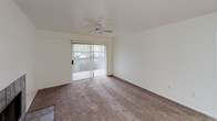 This single-floor residential unit offers a clean, functional layout with a variety of practical features throughout. The galley-style kitchen is well-appointed with light wood cabinetry, white countertops, a double-coil electric range, a refrigerator, a dishwasher, and a stainless single-basin sink. Tile flooring and a skylight-style flush ceiling fixture keep the space bright and easy to maintain. A pass-through counter connects the kitchen to the main living area, which features wall-to-wall carpeting, built-in shelving, and a tiled fireplace — adding both storage and a cozy focal point to the room. The living area opens to the outdoors through a sliding glass door with vertical blinds, bringing in natural light and providing access to an outdoor patio or balcony. The bedroom is generously sized, also carpeted, and includes its own sliding glass door with outdoor access, as well as a ceiling fan for comfortable airflow. The bathroom is neatly finished with tile flooring, a white vanity with under-sink storage, a large mirror with a lighted bar fixture above, and a shower/tub enclosure. Overall, the unit presents a bright, neutral palette throughout, offering a comfortable and move-in ready living environment.