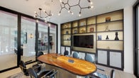 Located in the heart of Los Angeles' Arts District at 950 E Third St, this stylish conference room combines contemporary design with functional elegance. The centerpiece of the space is a stunning live-edge hardwood conference table, surrounded by sleek black and gold chairs, anchored atop a layered area rug that adds texture and warmth to the polished tile flooring.

A bold, branch-inspired chandelier with exposed Edison-style globe bulbs serves as a dramatic overhead focal point, casting a warm, ambient glow throughout the room. One full wall is dedicated to a built-in shelving unit finished in dark charcoal and gold tones, housing curated décor and a large flat-screen display — ideal for presentations and collaborative meetings.

Floor-to-ceiling black-framed glass partitions and sliding doors define the room's boundaries while maintaining a strong visual connection to the adjacent common area, allowing natural light to flow freely throughout. On the opposite side, expansive glazed walls look out onto a light-filled stairwell and exterior courtyard, reinforcing the open, airy feel of the space.

The overall ambiance is modern and professional, with a curated aesthetic that blends industrial and contemporary influences — making this conference room a standout setting for meetings, presentations, or collaborative work sessions.
