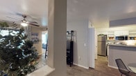 This single-floor residence offers a thoughtfully arranged open layout that connects the main living areas with ease and functionality. The interior is anchored by warm wood-look flooring that runs throughout, complementing the neutral gray and white wall tones that give the space a clean, contemporary feel.

A structural column near the entryway creates a natural visual division between the living and kitchen zones while maintaining an open sense of flow. The kitchen is equipped with stainless steel appliances, including a full-size refrigerator, and features crisp white cabinetry that maximizes both storage and brightness. The space transitions smoothly from the kitchen toward a hallway that connects the remaining rooms.

A dedicated shelving unit provides additional storage and display space along the main corridor, adding a functional yet stylish element to the interior. The bedroom, visible through the open layout, is well-lit with natural light filtering through curtained windows, contributing to a bright and welcoming ambiance. A ceiling fan in the bedroom adds comfort and practicality.

Overall, the residence presents a cohesive, move-in ready environment with consistent finishes, efficient use of space, and a calm, neutral palette that makes it versatile and easy to personalize.