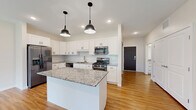 This well-appointed one-bedroom, one-bathroom unit in Delano, MN offers a thoughtfully designed single-floor layout with a clean, modern aesthetic throughout. Warm hardwood-style flooring flows through the main living areas, complemented by neutral tones and abundant natural light from multiple windows.

The open-concept kitchen and living room serves as the heart of the unit, featuring a granite-topped center island with dual pendant lighting, crisp white shaker cabinetry, a subway tile backsplash, stainless steel appliances — including a gas range, dishwasher, refrigerator, and microwave — and recessed lighting. The living area offers direct access to a private balcony overlooking lush, mature trees, providing a tranquil outdoor retreat.

The bedroom is carpeted for comfort and includes a large window with serene wooded views and a ceiling fan. A versatile den with hardwood-style flooring offers flexible use as a home office or additional living space. Two closets provide generous storage throughout the unit.

The bathroom is finished with a granite-topped white vanity, hardwood-style flooring, and a full tub/shower combo. Additional conveniences include a dedicated laundry area and utility room. The wide entryway corridor with built-in closet storage creates a welcoming arrival experience.