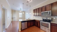 Located at 10800 McCombs St in El Paso, TX, this one-bedroom, one-bathroom unit offers a well-designed single-floor layout that makes efficient use of its space. The kitchen serves as a central highlight, featuring rich dark wood cabinetry extending to the ceiling, granite countertops, a subway tile backsplash, and a full suite of stainless steel appliances including a refrigerator, electric range, microwave, and dishwasher. A peninsula with pendant lighting overhead creates a natural divide between the kitchen and the adjacent living area, which includes a ceiling fan and a window that brings in natural light. Crown molding adds a refined architectural detail throughout the main living spaces. Wood-look tile flooring runs through the kitchen and living areas, lending warmth and durability. The bedroom is carpeted and features a ceiling fan, a window with blinds offering outdoor views, and access to a dedicated closet. The bathroom is finished with granite countertops, dark wood vanity cabinetry, and a tub/shower combination with floor-to-ceiling stone-look tile surround. Overall, the unit presents a clean, functional design with quality finishes throughout.
