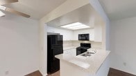 This single-floor space is designed with functionality and style in mind. The kitchen serves as a central highlight, featuring crisp white cabinetry that extends to the ceiling and provides ample storage. A peninsula with light granite countertops offers additional workspace and creates a natural division between the kitchen and the adjoining area, making it ideal for casual dining or entertaining. The kitchen is equipped with a full suite of black appliances, including a refrigerator, gas range, over-the-range microwave, and a stainless steel sink. A recessed skylight panel overhead floods the cooking area with natural light, enhancing the bright, airy atmosphere created by the white walls and cabinetry. The clean lines and neutral color palette throughout give the space a timeless, modern feel. Hardwood-style flooring adds warmth and continuity, grounding the overall aesthetic. The open sightlines and thoughtful layout make the space feel welcoming and practical, catering to everyday living with ease.