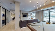 Located at 100 N Addison Ave in Elmhurst, IL, this thoughtfully designed single-floor amenity space offers a diverse range of gathering areas suited for both casual socializing and more structured entertaining. The open layout connects several distinct zones, each with its own character and function.

At the heart of the space is a striking gourmet kitchen anchored by an expansive marble-topped island with seating for multiple guests. Deep green cabinetry, open wood shelving, a bold geometric tile backsplash, stainless steel range hood, and schoolhouse pendant lighting combine to create a functional yet visually compelling culinary hub.

Adjacent to the kitchen, the main lounge area features light hardwood flooring, a built-in entertainment center with shelving and cabinetry, large windows that invite natural light, and a generously sized sectional sofa. A billiards table and a sculptural multi-arm chandelier add a playful, upscale touch to this gathering zone.

A separate, more intimate lounge is anchored by a classic white-tiled fireplace, complemented by a leather sofa, layered rugs, and curated artwork, offering a warm and inviting retreat.

The dining nook is defined by a solid wood communal table, tufted leather banquette seating, eclectic pendant lighting, and a gallery wall, creating an engaging space ideal for group meals or game nights. Herringbone tile flooring transitions seamlessly throughout the dining and kitchen areas, grounding the overall design with sophisticated texture.