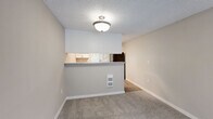 Located at 309 NE Fairgrounds Rd in Bremerton, WA, this two-bedroom, one-bathroom residence offers a well-organized single-floor layout with a clean, neutral aesthetic throughout. The combined kitchen and living area serves as the heart of the home, with a pass-through breakfast bar connecting the two spaces. The kitchen is equipped with white cabinetry, gray countertops, black appliances including an electric range and refrigerator, and wood-look flooring that adds warmth underfoot. The living room features plush carpet, a striking slate-tiled fireplace, and a sliding glass door that opens onto a private balcony with outdoor views. Both bedrooms are carpeted and receive natural light through blinded windows, with the primary bedroom offering a comfortable, well-proportioned retreat. Three closets provide ample storage throughout the unit. The bathroom features a full tub-shower combination, a white vanity with gray countertop, and wood-look flooring that mirrors the kitchen. A hallway connects the private areas of the home, and a textured ceiling is present throughout. The overall ambiance is bright, clean, and move-in ready.