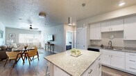 This thoughtfully designed 2-bedroom, 2-bathroom residence offers a practical and comfortable single-floor layout. The open-concept kitchen and living area serves as the heart of the home, anchored by a central granite-topped island with bar seating — ideal for casual dining or entertaining. White shaker cabinetry, stainless steel appliances, and pendant lighting give the kitchen a clean, modern aesthetic, while light wood-look flooring ties the space together seamlessly.

The living room is bright and welcoming, featuring large windows that invite generous natural light and a ceiling fan for year-round comfort. Neutral tones and a textured ceiling add warmth and depth to the space.

Both bedrooms are carpeted and well-sized, with ample natural light from windows dressed in blinds and drape panels. The primary bedroom connects to a private en-suite bathroom with a double-sink vanity, white cabinetry, and light quartz countertops. The second bathroom features a tub-shower combination with a single vanity, maintaining the same clean, contemporary style.

Two closets provide plentiful storage throughout the home. A dedicated in-unit laundry area houses a stacked washer and dryer, adding everyday convenience. The overall design palette — soft neutrals, crisp whites, and light wood tones — creates a cohesive and inviting atmosphere throughout.