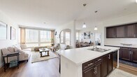 This well-appointed 2-bedroom, 3-bathroom residence in San Diego, CA offers a thoughtfully designed single-floor layout with generous living space. The open-concept living, dining, and kitchen area serves as the heart of the home, bathed in natural light through large windows and glass doors that frame views of the surrounding greenery. Light wood-tone flooring flows throughout the main living areas, lending warmth and continuity.

The kitchen is a standout feature, boasting rich dark cabinetry, stainless steel appliances, and a large white quartz island with bar seating — ideal for both cooking and casual dining. Pendant lighting above the island adds a refined touch. The adjacent dining area opens to a private balcony through French doors, creating a seamless indoor-outdoor connection.

The primary bedroom is a comfortable retreat with plush carpet, natural light from a dedicated window, and access to a spacious walk-in closet outfitted with multi-tiered shelving. The bathrooms are finished with elegant tile work, including a full tub-shower combination featuring marble-style tile surround and wood-look flooring. The second bedroom is equally inviting, with carpet flooring and bright windows. A dedicated hallway with a dark wood double vanity connects the living spaces with ease.