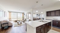 This well-appointed 2-bedroom, 3-bathroom residence in San Diego, CA offers a thoughtfully designed single-floor layout with generous living space. The open-concept living, dining, and kitchen area serves as the heart of the home, bathed in natural light through large windows and glass doors that frame views of the surrounding greenery. Light wood-tone flooring flows throughout the main living areas, lending warmth and continuity.

The kitchen is a standout feature, boasting rich dark cabinetry, stainless steel appliances, and a large white quartz island with bar seating — ideal for both cooking and casual dining. Pendant lighting above the island adds a refined touch. The adjacent dining area opens to a private balcony through French doors, creating a seamless indoor-outdoor connection.

The primary bedroom is a comfortable retreat with plush carpet, natural light from a dedicated window, and access to a spacious walk-in closet outfitted with multi-tiered shelving. The bathrooms are finished with elegant tile work, including a full tub-shower combination featuring marble-style tile surround and wood-look flooring. The second bedroom is equally inviting, with carpet flooring and bright windows. A dedicated hallway with a dark wood double vanity connects the living spaces with ease.