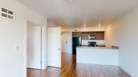 This efficient 2-bedroom, 1-bathroom unit is designed with a clean, modern aesthetic and a practical single-floor layout. The open-concept kitchen and living area forms the heart of the unit, anchored by a peninsula-style kitchen island with a double stainless steel sink and neutral countertops. Dark walnut-toned cabinetry lines the kitchen walls, complemented by black appliances including a refrigerator, electric range, and over-the-range microwave. Warm hardwood-style flooring runs continuously throughout the entire unit, lending cohesion and a sense of warmth to every room. Recessed lighting illuminates the kitchen and living area, which flows openly to allow for flexible furniture arrangements. The primary bedroom offers a comfortable footprint with a ceiling fan, a large window framing outdoor greenery and natural light, and ample wall space. The second bedroom is a well-proportioned room with hardwood-style flooring and built-in ventilation. The bathroom features matching hardwood-style flooring, a clean white palette, and functional fixtures. The unit also includes a utility closet area. Overall, the space presents a straightforward, move-in-ready layout with consistent finishes and a bright, neutral color scheme throughout.