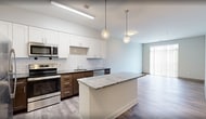 Unit 309 at 701 N 1st Street in Richmond, VA is a 780-square-foot, two-bedroom, two-bathroom apartment designed with modern finishes throughout. The open kitchen and living area serves as the heart of the unit, featuring a well-appointed kitchen with stainless steel appliances including a refrigerator, electric range, and built-in microwave. Two-tone cabinetry pairs white upper cabinets with dark lower cabinets, complemented by dark granite countertops and a classic white subway tile backsplash. A kitchen island provides additional counter and storage space. Wood-style plank flooring runs consistently throughout the entire unit, adding warmth and visual continuity. The primary bedroom measures 160 square feet and includes direct access to an en-suite bathroom and a dedicated walk-in closet with wire shelving. The second bedroom offers comparable comfort with access to the second full bathroom. Both bathrooms are finished with large-format tile surrounds in the tub/shower combinations and dark wood vanity cabinetry with light countertops. Neutral gray walls and two-panel interior doors complete the clean, contemporary aesthetic of this thoughtfully designed apartment.