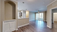 Located at 5827 Legacy Crescent Pl in Riverview, FL, this single-floor residence offers a well-designed open-concept layout that seamlessly connects the kitchen, dining, and living areas. The kitchen is a standout feature, equipped with stainless steel appliances including a gas range, microwave, and bold range hood. Dark taupe cabinetry is complemented by light quartz countertops and a mosaic tile backsplash, while a peninsula with a built-in sink adds both function and style. Tile flooring grounds the kitchen, transitioning to warm hardwood-style flooring throughout the rest of the home. The living area is bright and inviting, with a ceiling fan, crown molding, and large sliding glass doors fitted with vertical blinds that open to an outdoor balcony with greenery views. The bedrooms are comfortably sized, each with ceiling fans and ample natural light from large windows. One bedroom features a spacious walk-in closet with wire shelving for generous storage. The bathroom is cleanly finished with large-format white tile in the tub surround, accented by a decorative mosaic border, and complemented by dark cabinetry. Throughout the home, neutral beige tones and consistent trim work create a cohesive, move-in-ready aesthetic.
