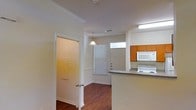 This two-story space in Denton, Texas offers a practical and comfortable layout with thoughtful design details throughout. The main level showcases rich hardwood-style flooring that runs through the open living and kitchen areas, adding warmth and visual continuity to the space.

The kitchen is positioned in an open-concept arrangement, featuring warm medium-toned wood cabinetry paired with grey countertops and a raised breakfast bar that provides a natural division between the kitchen and adjacent areas. White appliances, including an electric range and over-the-range microwave, are neatly integrated into the cabinetry. A transom window above the kitchen area allows additional natural light to filter in, brightening the workspace.

A pendant light fixture hangs above, contributing both ambient and task lighting to the open area. Crown molding along the ceiling adds a polished architectural touch throughout the main level. A doorway with a closet nearby provides convenient storage access. Blinds on the windows offer light control while maintaining privacy.

The overall ambiance is clean, neutral, and functional, with a straightforward design that provides a solid foundation for personalization.