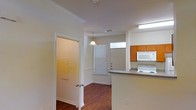 This two-story space in Denton, Texas offers a practical and comfortable layout with thoughtful design details throughout. The main level showcases rich hardwood-style flooring that runs through the open living and kitchen areas, adding warmth and visual continuity to the space.

The kitchen is positioned in an open-concept arrangement, featuring warm medium-toned wood cabinetry paired with grey countertops and a raised breakfast bar that provides a natural division between the kitchen and adjacent areas. White appliances, including an electric range and over-the-range microwave, are neatly integrated into the cabinetry. A transom window above the kitchen area allows additional natural light to filter in, brightening the workspace.

A pendant light fixture hangs above, contributing both ambient and task lighting to the open area. Crown molding along the ceiling adds a polished architectural touch throughout the main level. A doorway with a closet nearby provides convenient storage access. Blinds on the windows offer light control while maintaining privacy.

The overall ambiance is clean, neutral, and functional, with a straightforward design that provides a solid foundation for personalization.