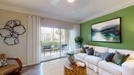 This single-floor residence offers a thoughtfully designed layout that balances comfort and style. The living room serves as the heart of the home, featuring crown molding, wood-look flooring, and a bold green accent wall adorned with landscape artwork. A set of sliding glass doors floods the space with natural light and opens directly onto a private patio, ideal for outdoor relaxation. The adjacent dining area continues the green accent wall theme, accented by a triptych of botanical prints above a clean, modern dining table.

The kitchen is outfitted with white shaker cabinetry, subway tile backsplash, and a full suite of stainless steel appliances, including a range, over-the-range microwave, and refrigerator — providing both functionality and a sleek aesthetic.

The bedrooms are carpeted and serene, each offering ample space, ceiling fans, and soft neutral tones. The primary bedroom connects directly to a private en-suite bathroom, while a second bathroom features wood-look flooring, a wide vanity with white cabinetry, and a bathtub. A dedicated laundry area with a full-size washer and dryer, accompanied by built-in wire shelving for storage, adds everyday convenience to this well-rounded home.
