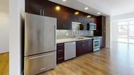 This single-floor residence offers a thoughtfully designed open-concept layout that seamlessly connects the kitchen and living areas. The kitchen is a standout feature, showcasing floor-to-ceiling dark espresso cabinetry with sleek bar-pull hardware, light quartz countertops, and a classic subway tile backsplash. A full suite of stainless steel appliances — including a gas range, over-the-range microwave, dishwasher, and refrigerator — provides a polished, contemporary aesthetic. Recessed lighting and under-cabinet fixtures ensure the kitchen is both functional and well-lit.

The open living area extends generously from the kitchen, bathed in natural light through large floor-to-ceiling windows that frame outdoor views of the surrounding neighborhood. Warm wood-style flooring flows consistently throughout the living spaces and bedrooms, contributing to a cohesive and inviting atmosphere.

The bedrooms are bright and airy, each featuring windows that draw in natural light, with louvered closet doors offering practical storage solutions. The bathroom maintains the home's clean, modern design language with dark cabinetry, light countertops, tile flooring, and a glass-enclosed tub-shower combination. Throughout, the crisp white walls and contemporary finishes create a bright, minimalist ambiance.