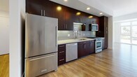 This single-floor residence offers a thoughtfully designed open-concept layout that seamlessly connects the kitchen and living areas. The kitchen is a standout feature, showcasing floor-to-ceiling dark espresso cabinetry with sleek bar-pull hardware, light quartz countertops, and a classic subway tile backsplash. A full suite of stainless steel appliances — including a gas range, over-the-range microwave, dishwasher, and refrigerator — provides a polished, contemporary aesthetic. Recessed lighting and under-cabinet fixtures ensure the kitchen is both functional and well-lit.

The open living area extends generously from the kitchen, bathed in natural light through large floor-to-ceiling windows that frame outdoor views of the surrounding neighborhood. Warm wood-style flooring flows consistently throughout the living spaces and bedrooms, contributing to a cohesive and inviting atmosphere.

The bedrooms are bright and airy, each featuring windows that draw in natural light, with louvered closet doors offering practical storage solutions. The bathroom maintains the home's clean, modern design language with dark cabinetry, light countertops, tile flooring, and a glass-enclosed tub-shower combination. Throughout, the crisp white walls and contemporary finishes create a bright, minimalist ambiance.