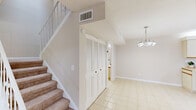 Located in Stuart, FL, this two-story home offers a practical and well-organized layout spread across two floors. The main level features light-toned tile flooring throughout, anchored by a combined kitchen and dining area. The kitchen is equipped with ample cream cabinetry trimmed in wood, generous counter space, and a double sink, providing an efficient and functional cooking environment. The adjacent dining area is illuminated by a chandelier, creating a welcoming atmosphere. A louvered-door closet near the base of the staircase adds convenient main-level storage. Also on the main floor, a dedicated laundry room houses a full-size washer and dryer with overhead wire shelving. A carpeted staircase with a classic white balustrade leads to the upper level, where both bedrooms are found. Each bedroom features soft carpeting, a ceiling fan with light kit, and a neutral color palette that promotes a calm and restful environment. The generously sized primary bedroom offers ample room for furnishings. The full bathroom features a wide vanity with dual sinks, wood-accented cabinetry, and a skylight-style overhead panel that introduces natural light. The home's consistent neutral tones and clean finishes throughout create a cohesive and comfortable living environment.