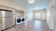 Located at 1901 Vine St in Kansas City, MO, this two-bedroom, two-bathroom residence offers a well-designed single-floor layout with contemporary finishes throughout. The living room is bright and open, featuring light wood-look vinyl plank flooring, large windows that invite natural light, and a glass-panel exterior door providing additional illumination and outdoor access. The kitchen is outfitted with light wood cabinetry, white quartz countertops, a subway tile backsplash, stainless steel appliances including a range, dishwasher, and refrigerator, plus recessed lighting overhead. Both bedrooms are carpeted and feature windows with views to the outdoors, offering a comfortable and quiet retreat. The generously sized primary bedroom connects to a bathroom with a light wood vanity, illuminated mirror, white countertop, and a shower-tub combo. The second bathroom provides an accessible walk-in shower with grab bar support and a separate vanity. A dedicated in-unit laundry area accommodates a full-size washer and dryer side by side. Additional storage is provided by a carpeted walk-in closet with wire shelving. Neutral tones and consistent flooring create a cohesive, modern ambiance throughout the home.