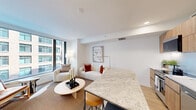 This thoughtfully designed single-floor residence offers a clean, contemporary aesthetic defined by a neutral palette, light wood flooring, and an abundance of natural light. The open-concept living area serves as the heart of the home, featuring floor-to-ceiling windows that frame urban skyline views and fill the space with daylight. The living room provides a comfortable and stylish setting with ample room for seating arrangements.

The kitchen is outfitted with flat-front wood-tone cabinetry, white quartz countertops, stainless steel appliances including a range, dishwasher, and refrigerator, and a spacious granite-topped island that doubles as a casual dining and entertaining surface. Under-cabinet lighting adds a polished touch.

A wide hallway with light wood flooring connects the main living areas to the private quarters, which include two bedrooms. The primary bedroom features a sliding-door closet with built-in organization, while the second bedroom also offers generous closet storage. Both rooms are bright and serene.

The bathroom is finished with a floating wood vanity, white countertop, and a backlit mirror, creating a spa-like atmosphere. The overall design balances functionality with modern elegance throughout.