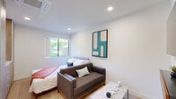Located at 7810 Topanga Canyon Boulevard in Los Angeles, CA, this efficiently designed one-bedroom, one-bathroom unit offers a clean, modern aesthetic throughout its single floor. The layout connects a hallway, kitchen, bathroom, and a spacious primary bedroom in a well-organized floor plan.

The bedroom serves as the heart of the unit, functioning as both a sleeping and living area. Light wood-style flooring, recessed lighting, and crisp white walls create a bright, airy atmosphere. A window provides natural light and a view of outdoor greenery, while a wall-mounted TV and floating wood shelf add functional, contemporary touches. A compact sofa and coffee table define a sitting area within the room.

The kitchen is well-appointed with dark espresso cabinetry, white countertops, and a full suite of stainless steel appliances including a gas range, over-the-range microwave, dishwasher, and full-size refrigerator. Light wood flooring continues throughout, maintaining a cohesive look.

The bathroom features a long, streamlined vanity with warm wood cabinetry and a white countertop, an illuminated mirror, a glass-enclosed shower, and a toilet — all finished in a clean, minimal style consistent with the rest of the unit. The overall ambiance is modern, functional, and well-maintained.