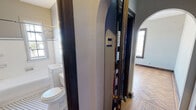 Located at 814 W Hill Ave in Knoxville, Tennessee, this single-floor unit blends classic architectural character with functional design. The space is defined by warm parquet wood flooring that runs throughout, complemented by rich dark wood trim, arched doorways, and built-in shelving that add a timeless, historic charm.

The main room is open and airy, benefiting from large, dark-trimmed windows that invite natural light and offer views of the surrounding neighborhood. A ceiling fan provides overhead comfort, and a wall-mounted HVAC unit ensures climate control. Two hallways connect the space efficiently, maintaining a logical flow throughout.

The kitchenette is neatly tucked behind arched cabinetry doors and features tile countertops, a stainless steel sink, a compact refrigerator, and overhead shelving with a microwave — offering essential cooking amenities in a well-organized, compact layout. A textured wood-paneled backsplash adds visual warmth to the kitchen area.

The bathroom retains its classic character with white subway tile walls accented by blue trim, a combination tub and shower, a single vanity with sink, and a window that allows natural light to brighten the space. A patterned tile floor adds a vintage touch that ties into the overall historic aesthetic of the unit.