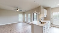 Located on Johns Island, SC, this single-story home showcases a clean, modern design with an open-concept floor plan that seamlessly connects the main living areas. Light neutral tones, crisp white trim, and luxury vinyl plank flooring run throughout, creating a bright and cohesive aesthetic.

The kitchen is a standout feature, equipped with white shaker cabinetry accented by matte black hardware, a peninsula with a single-basin sink and pendant lighting above, quartz countertops, and stainless steel appliances including a refrigerator with ice maker, range, and microwave. A door from the kitchen provides direct outdoor access.

The open living area is generously proportioned, filled with natural light from multiple windows with blinds, and finished with a ceiling fan. A wide hallway connects the living spaces to the private areas of the home, maintaining a sense of flow throughout.

The bathrooms feature white vanity cabinetry with quartz countertops, matte black hardware, framed mirrors, and tiled walk-in showers with glass doors. The dedicated laundry area includes a full-size top-loading washer and dryer with overhead wire shelving for additional storage. The home's bright, move-in-ready condition and thoughtful layout make it a well-appointed residence in the growing Johns Island community.