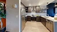 Located in Henderson, NV, this well-appointed one-bedroom, one-bathroom residence offers a thoughtfully designed open-concept layout with modern finishes throughout. The living area flows naturally into the kitchen, which serves as a focal point of the home, featuring dark wood cabinetry, open shelving, stainless steel appliances including a full-size refrigerator and range with a wall-mounted hood, light quartz countertops, and a large undermount sink set into a breakfast bar — ideal for casual dining or entertaining.

The bedroom is a serene retreat, showcasing an exposed concrete ceiling that adds an industrial-chic character, plush carpet flooring, and large black-framed windows on multiple walls that invite abundant natural light and offer views of the surrounding Henderson landscape. A full-width mirrored sliding closet adds functionality while enhancing the sense of space.

The bathroom is sleek and modern, with light tile flooring, a dark accent wall, a floating wood vanity with a white basin, a backlit mirror, and curated artwork that adds a touch of personality. Light wood-style flooring runs through the main living areas, and colorful art pieces displayed throughout contribute to the space's vibrant, contemporary ambiance.