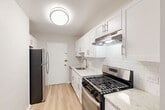 Located at 6166 Leesburg Pike in Falls Church, VA, this thoughtfully designed 2-bedroom, 2-bathroom residence offers a clean, modern aesthetic throughout its single-floor layout. The open living room is bright and airy, featuring light-toned hardwood-style flooring, neutral gray walls, and multiple windows dressed with vertical blinds that invite generous natural light. The space flows seamlessly into the kitchen, which is a standout feature with white shaker cabinetry, granite-style countertops, a subway tile backsplash, a stainless steel gas range, and a black refrigerator — all set atop matching light hardwood flooring. Both bedrooms are comfortably sized, with the spacious primary bedroom offering ample room for furnishings. The bedrooms are finished with plush carpeting, vertical-blind windows for natural light, and easy access to the three closets distributed throughout the unit. The bathrooms are clean and well-appointed, featuring white tiled tub-shower surrounds, granite-topped vanities, and white cabinetry. With a neutral color palette, updated finishes, and a practical layout, this residence offers a comfortable and modern living environment in a convenient Falls Church location.