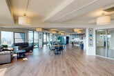 Located in the heart of Detroit's Midtown neighborhood, this generously sized amenity floor offers a well-rounded selection of community spaces spread across a single, thoughtfully designed level. Light hardwood flooring flows throughout, complemented by exposed beam ceilings and large floor-to-ceiling windows that bathe the interiors in natural light and frame sweeping panoramic views of the Detroit skyline.

The expansive community room serves as the centerpiece of the floor, featuring an open-plan layout with a lounge area furnished with leather seating, a dining area with a central table and chairs, and a full kitchen with dark wood cabinetry and a sink — ideal for gatherings and events. Glass-paneled doors allow visual connectivity between spaces while maintaining defined zones. A bar-height counter runs along a wall of windows, providing a sunlit perch with unobstructed city views.

A dedicated fitness center is enclosed in glass and equipped with cardio machines including a stationary bike, elliptical, and treadmill. Adjacent to it, a game area features a full-size ping pong table. The floor also includes a laundry facility, a patio for outdoor enjoyment, and a hallway connecting all areas. City artwork and framed prints add a local character throughout.